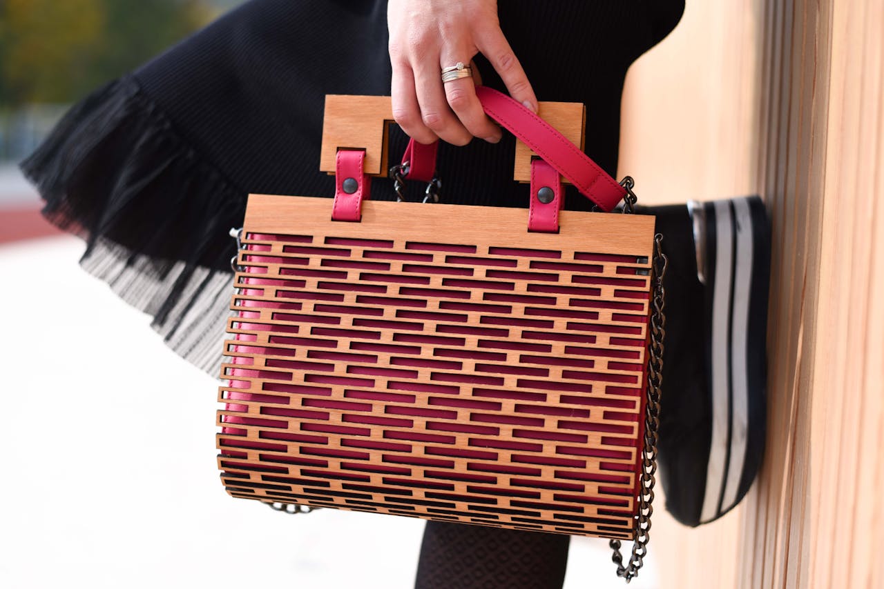 Elegant wooden handbag with red accents held by a person in fashionable attire.