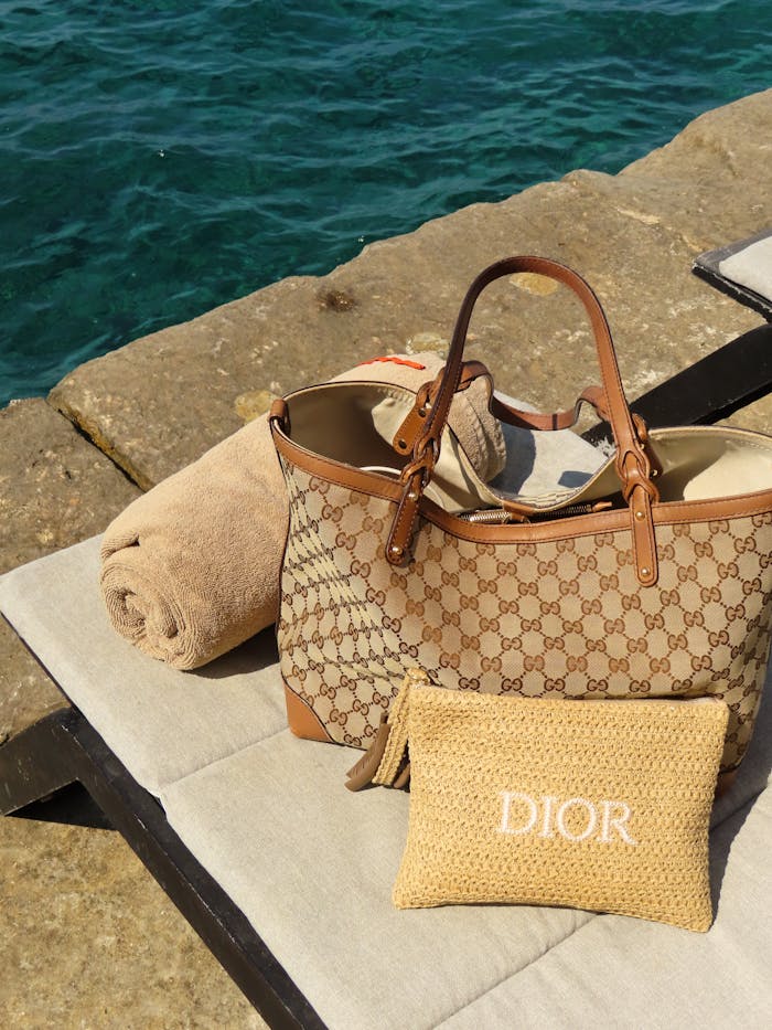 Elegant designer bags and towel by the ocean, perfect for a luxury beach day.